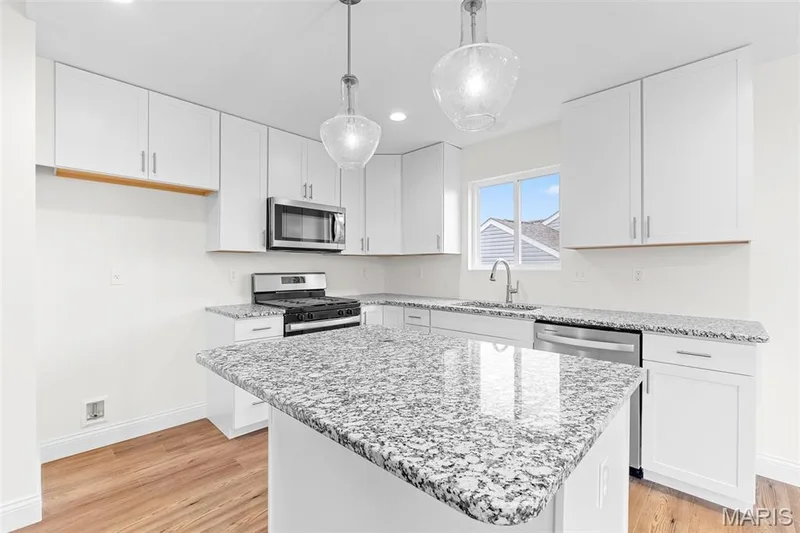 Kitchen with appliances with stainless steel finishes, light stone counters, light wood-style flooring, decorative light fixtures, and white cabinetry — 1 TBB Sydney @ Kreder Farms, St Charles, MO 63304