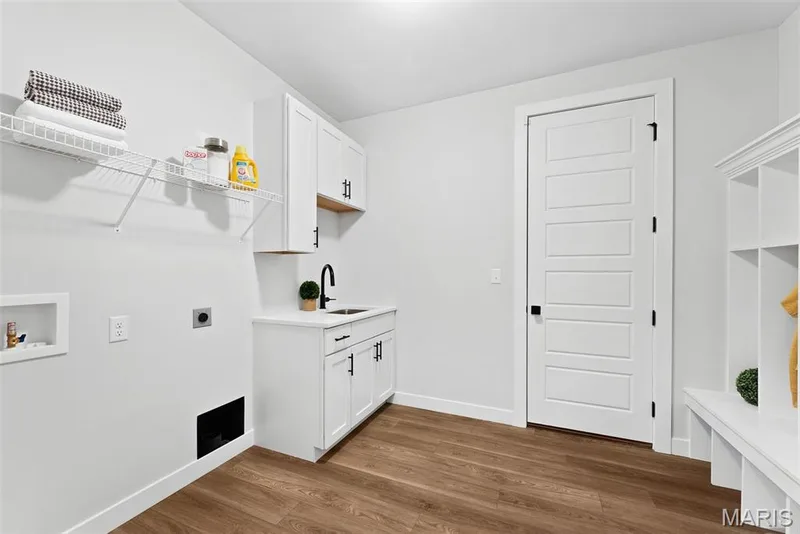 Laundry area featuring dark wood-style flooring, electric dryer hookup, washer hookup, and cabinet space — 1 TBB Canterbury @ Creekside Sommers, O'Fallon, MO 63367