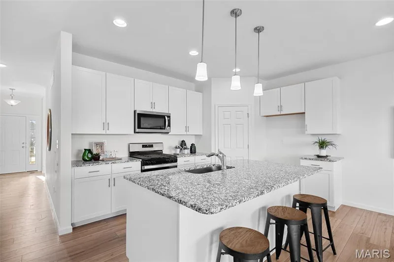 Kitchen with a breakfast bar area, white cabinets, hanging light fixtures, appliances with stainless steel finishes, and light stone counters — 1 TBB Westbrook @ Creekside Sommers, O'Fallon, MO 63367