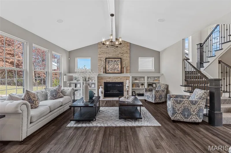 Living area featuring beamed ceiling, stairway, a stone fireplace, dark wood finished floors, and a chandelier — 1 TBB Kingston @Willow Grove, Dardenne Prairie, MO 63368