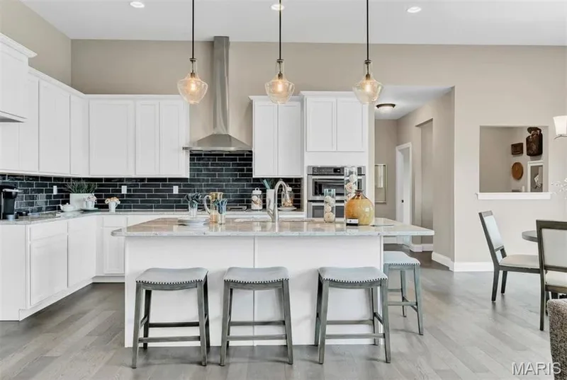 Kitchen featuring wall chimney range hood, light stone countertops, white cabinets, an island with sink, and recessed lighting — 1 TBB Monaco @ Chateau De Fond Du Lac, Lake St. Louis, MO 63367