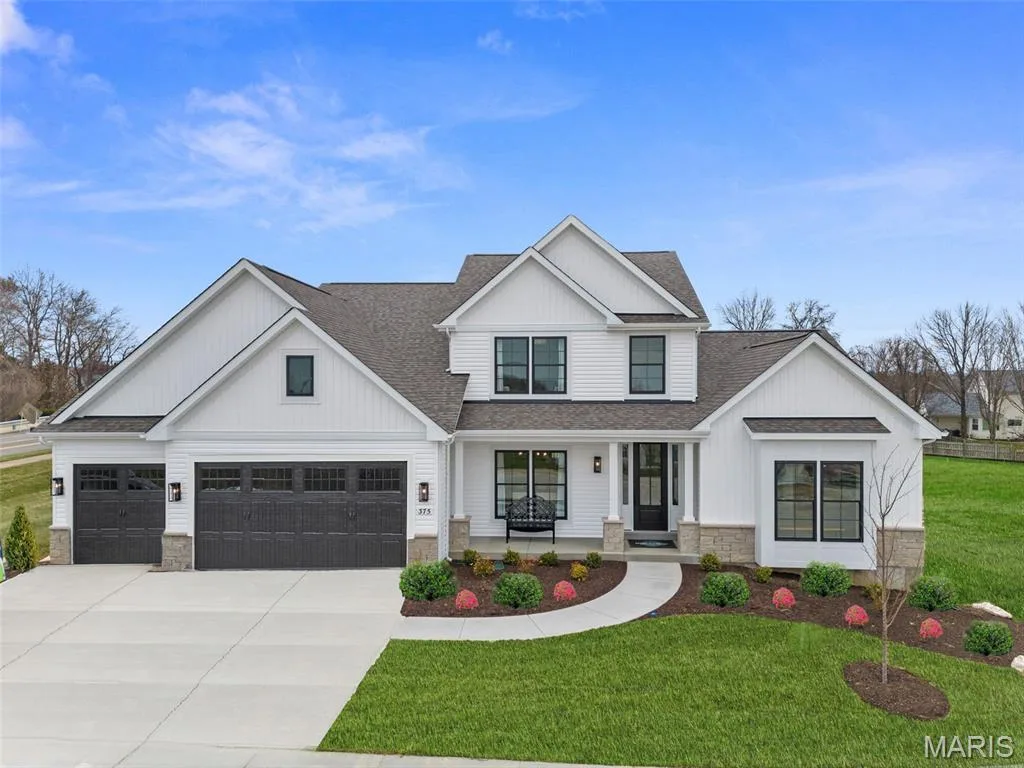 Modern inspired farmhouse featuring a shingled roof, a porch, stone siding, and concrete driveway — 1 TBB Bridgeport @Willow Grove, Dardenne Prairie, MO 63368