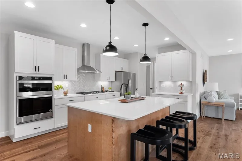 Kitchen with an island with sink, a kitchen breakfast bar, decorative backsplash, dark wood finished floors, and hanging light fixtures — 1 TBB Bridgeport @Willow Grove, Dardenne Prairie, MO 63368