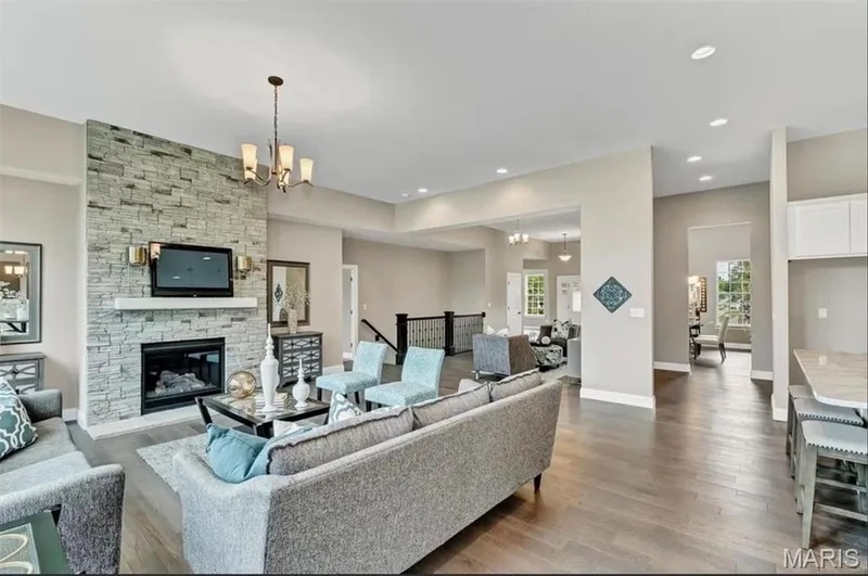 Living room with dark wood-style floors, a chandelier, recessed lighting, and a stone fireplace — 1 TBB Monaco @Willow Grove, Dardenne Prairie, MO 63368