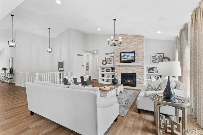 Living area featuring light wood-style flooring, a chandelier, high vaulted ceiling, a stone fireplace, and recessed lighting — 1 TBB Canterbury@ Willow Grove, Dardenne Prairie, MO 63368