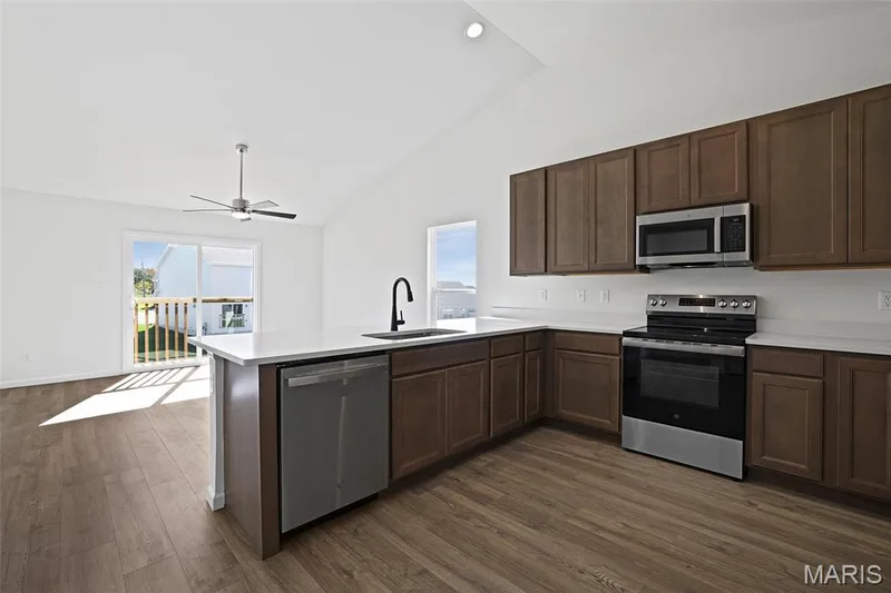 Kitchen featuring stainless steel appliances, light countertops, dark brown cabinets, dark wood finished floors, and a peninsula — 19 Integrity Court, O'Fallon, MO 63385
