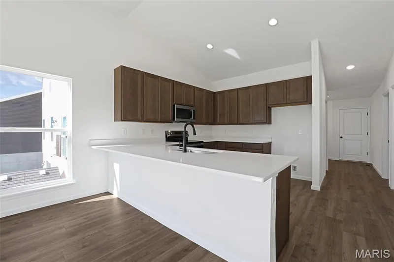 Kitchen featuring a peninsula, dark brown cabinets, dark wood-style flooring, appliances with stainless steel finishes, and recessed lighting — 19 Integrity Court, O'Fallon, MO 63385