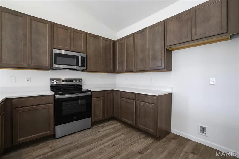 Kitchen with appliances with stainless steel finishes, dark brown cabinets, light countertops, dark wood finished floors, and lofted ceiling — 19 Integrity Court, O'Fallon, MO 63385