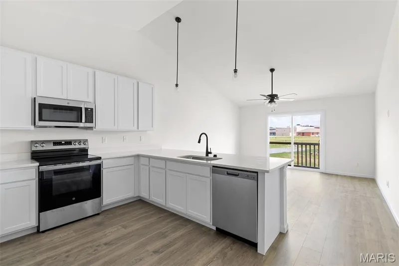 Kitchen featuring stainless steel appliances, vaulted ceiling, white cabinetry, light wood-type flooring, and a peninsula — 46 Integrity Court, O'Fallon, MO 63385