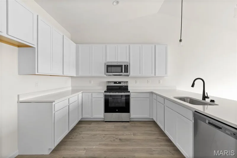 Kitchen featuring appliances with stainless steel finishes, lofted ceiling, light wood-style floors, hanging light fixtures, and white cabinets — 46 Integrity Court, O'Fallon, MO 63385