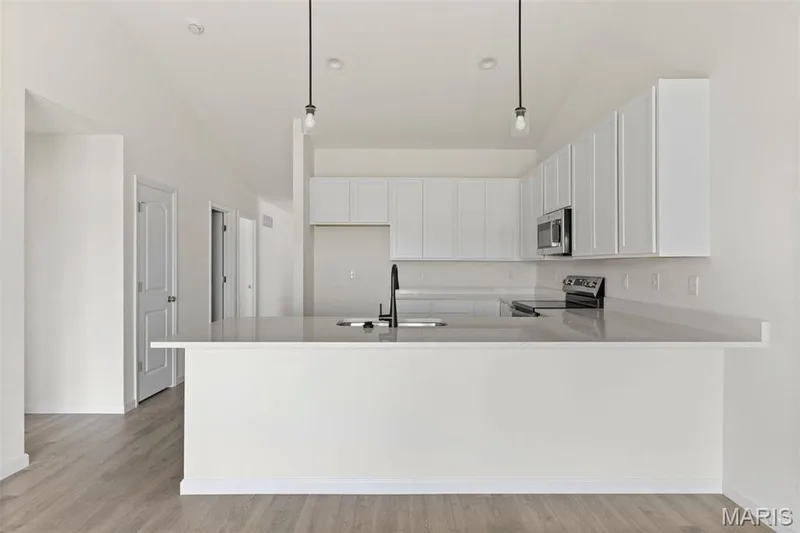 Kitchen with a peninsula, white cabinetry, decorative light fixtures, stainless steel appliances, and light wood finished floors — 46 Integrity Court, O'Fallon, MO 63385