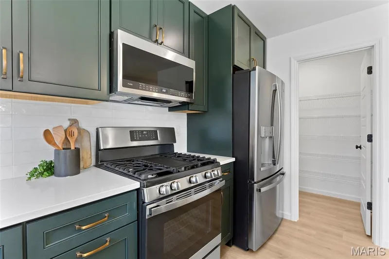 Kitchen with green cabinets, appliances with stainless steel finishes, light wood-type flooring, and backsplash — 3 Sterling at Westhaven, Wentzville, MO 63385