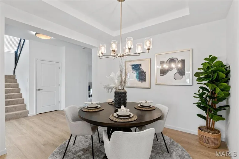 Dining space featuring light hardwood / wood-style floors, a tray ceiling, and a notable chandelier — 3 Ashford at Elm Crossing, St Charles, MO 63301