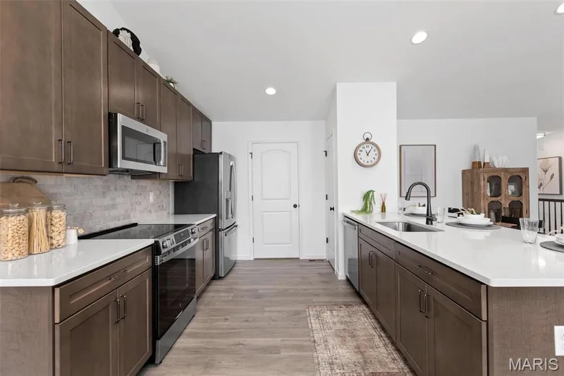 Kitchen with dark brown cabinets, sink, light hardwood / wood-style flooring, decorative backsplash, and appliances with stainless steel finishes — 3 Aspen at Elm Crossing, St Charles, MO 63301