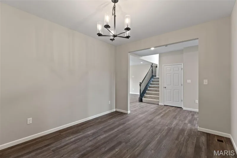 Unfurnished dining area with dark wood-style flooring, stairs, and a chandelier — 225 Windmill View Drive, O'Fallon, MO 63385