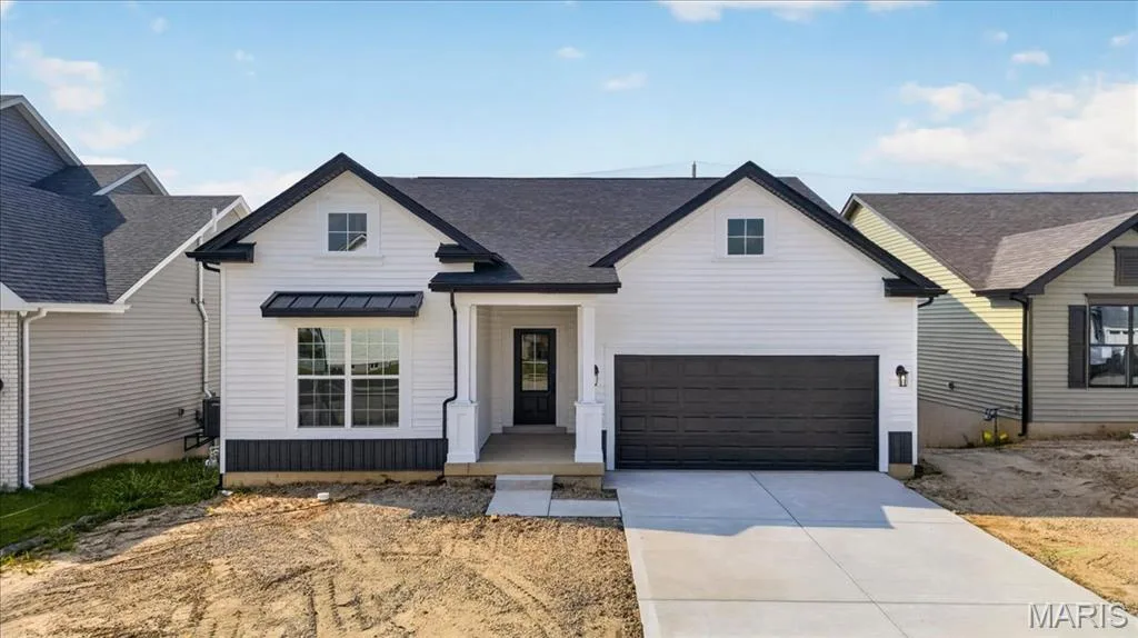 A striking modern farmhouse elevation featuring crisp white siding, bold black accents, decorative metal roof detail, and a welcoming covered front porch. Clean architectural lines and timeless curb appeal create an impressive first impression. — 86 River Wind Drive, St Charles, MO 63301