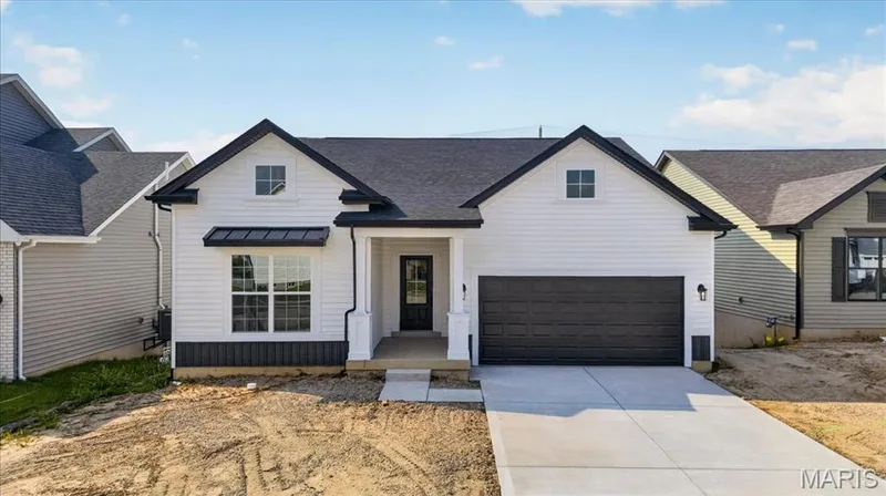 A striking modern farmhouse elevation featuring crisp white siding, bold black accents, decorative metal roof detail, and a welcoming covered front porch. Clean architectural lines and timeless curb appeal create an impressive first impression. — 86 River Wind Drive, St Charles, MO 63301