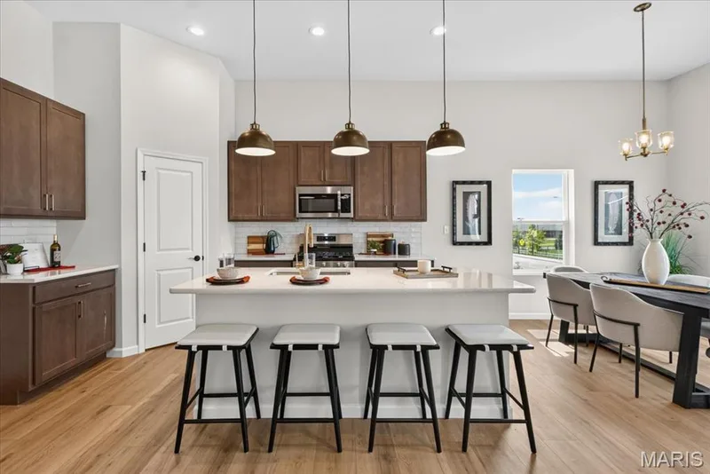 This light-filled kitchen showcases an expansive island perfect for gathering, designer cabinetry, quartz countertops, subway tile backsplash, and seamless access to the dining and living areas, making entertaining effortless. — 86 River Wind Drive, St Charles, MO 63301
