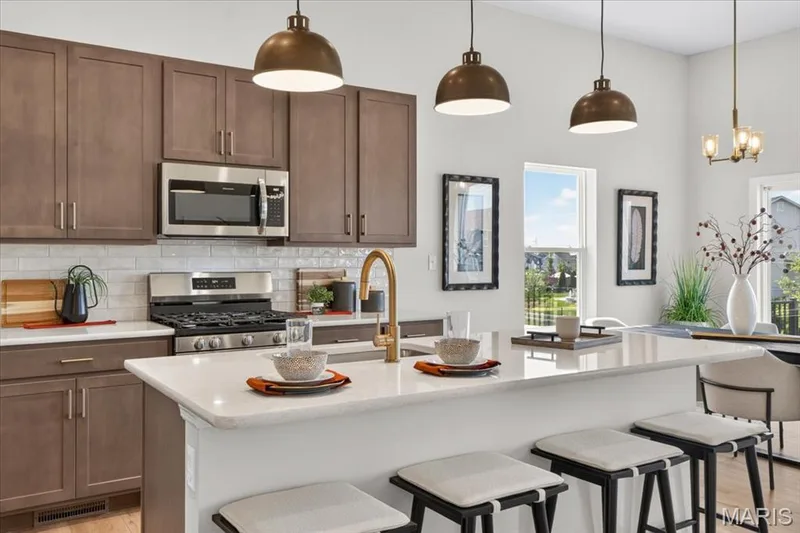 The chef-inspired kitchen combines beauty and functionality with ample workspace, premium quartz countertops, stainless steel appliances, a spacious center island with seating, and abundant cabinet storage to meet every culinary need. — 86 River Wind Drive, St Charles, MO 63301