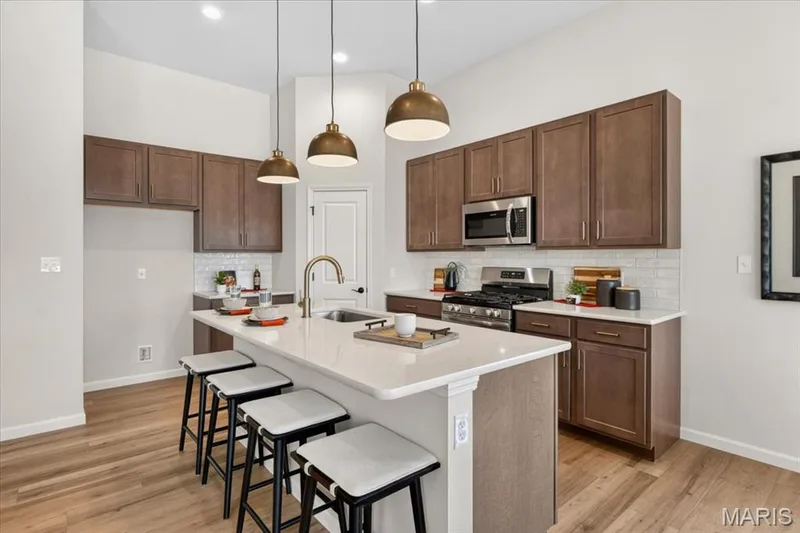 The stunning kitchen serves as the centerpiece of the home, featuring an oversized island with seating, beautiful quartz countertops, designer lighting, stainless steel appliances, a walk-in pantry, and an open-concept layout perfect for hosting family and friends. — 86 River Wind Drive, St Charles, MO 63301