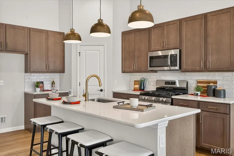 Built for today's lifestyle, the open-concept kitchen features a large island overlooking the main living areas, elegant pendant lighting, quartz countertops, a walk-in pantry, and plenty of space for family meals and entertaining. — 86 River Wind Drive, St Charles, MO 63301