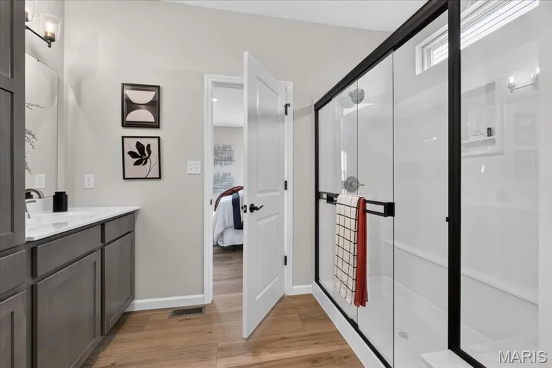 Unwind in the spa-inspired primary bath featuring dual vanities with abundant storage, a spacious walk-in shower with a sleek black-framed glass enclosure, and direct access to a generous walk-in closet for added convenience. — 86 River Wind Drive, St Charles, MO 63301
