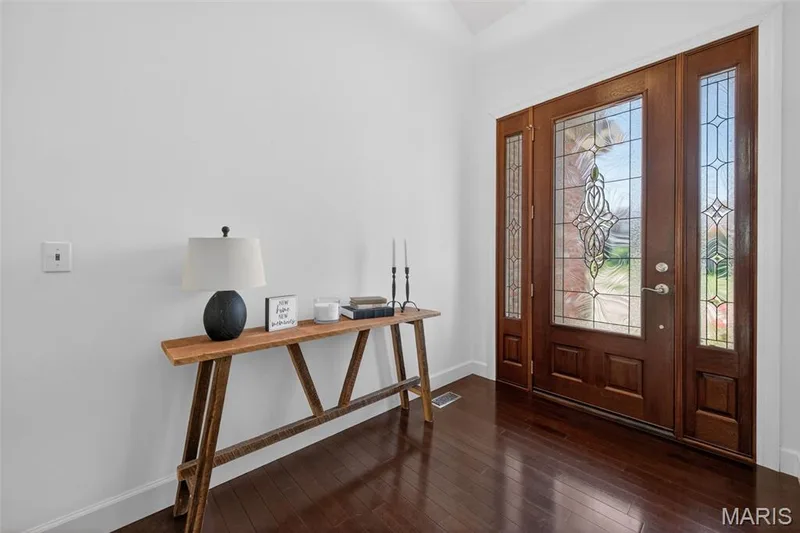 Entry foyer with vaulted ceiling, featuring rich wood-finish flooring and a decorative entry door with leaded glass panels — 216 Woodland Place Court, St Charles, MO 63303