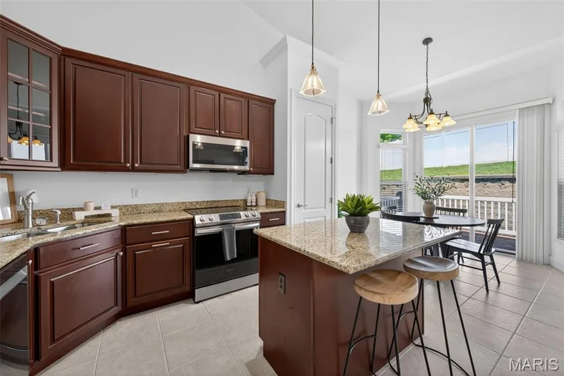 Kitchen featuring dark wood cabinetry, granite countertops, stainless steel appliances, and a central island with bar seating — 216 Woodland Place Court, St Charles, MO 63303