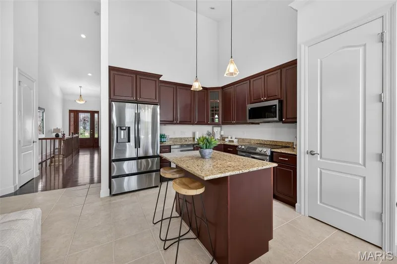 Kitchen featuring dark wood cabinetry, stainless steel appliances, and a central island with a light-toned granite countertop — 216 Woodland Place Court, St Charles, MO 63303