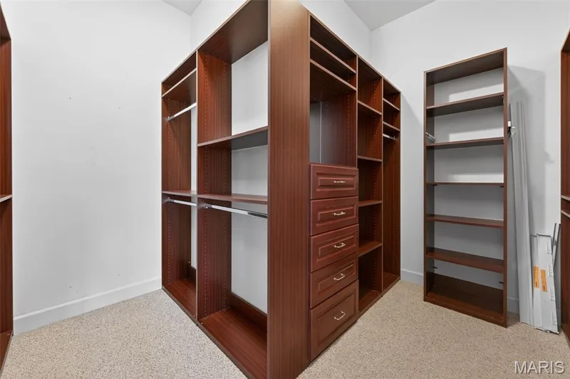 Expansive custom luxury closet system in the primary bedroom  featuring rich wood-finish cabinetry, integrated drawers, shelving, and hanging rods — 216 Woodland Place Court, St Charles, MO 63303