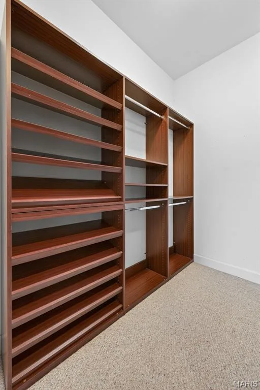 Custom luxury closet system in the primary bedroom featuring rich wood-finish shelving and metal hanging rods — 216 Woodland Place Court, St Charles, MO 63303