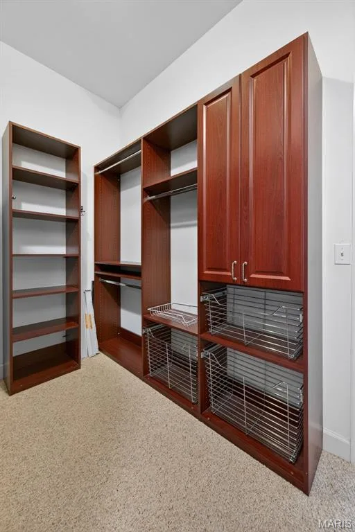 Custom walk in luxury closet in the primary bedroom featuring a rich wood-finish, multiple shelving units, integrated hanging rods, closed cabinetry, and pull-out wire baskets — 216 Woodland Place Court, St Charles, MO 63303
