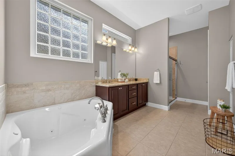 Renovated primary bathroom featuring a corner spa tub, a dual vanity with a granite countertops — 216 Woodland Place Court, St Charles, MO 63303