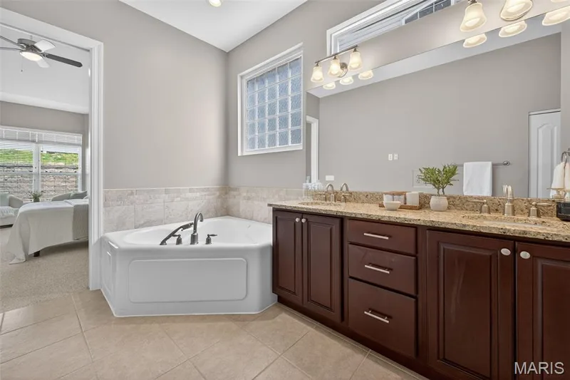 Spacious primary bathroom featuring a corner soaking tub, a dual vanity with a granite countertop, and tiled flooring — 216 Woodland Place Court, St Charles, MO 63303