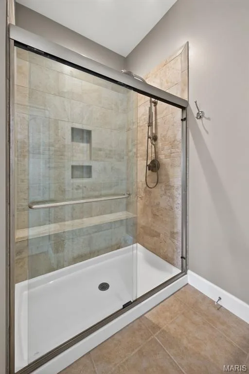 Primary bathroom shower with glass-enclosed doors,  luxury dual shower head, marble tiled walls and a built-in bench — 216 Woodland Place Court, St Charles, MO 63303