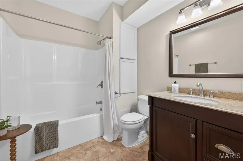 Full bathroom in the lower level featuring a white tub/shower combination, a dark wood-finish vanity with granite countertop — 216 Woodland Place Court, St Charles, MO 63303