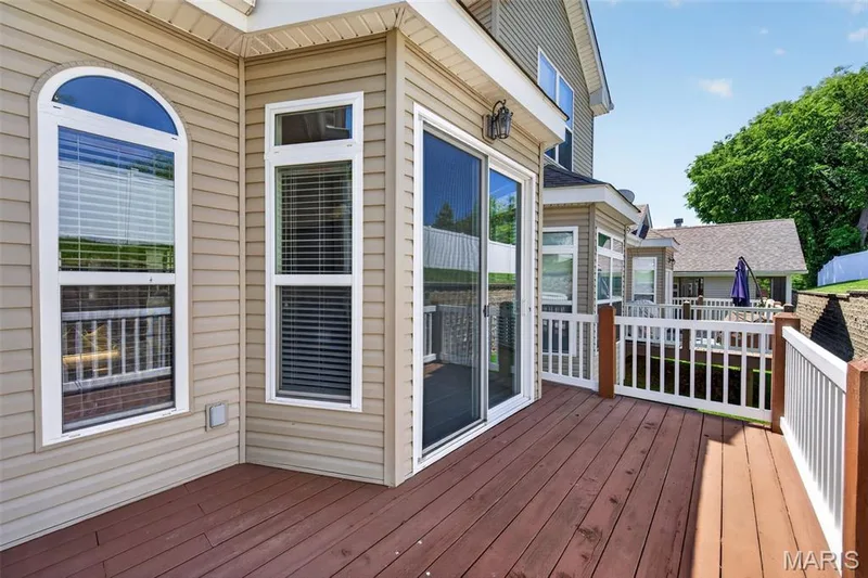 Spacious outdoor deck featuring rich wood-finish flooring, white railing, and a sliding glass door — 216 Woodland Place Court, St Charles, MO 63303
