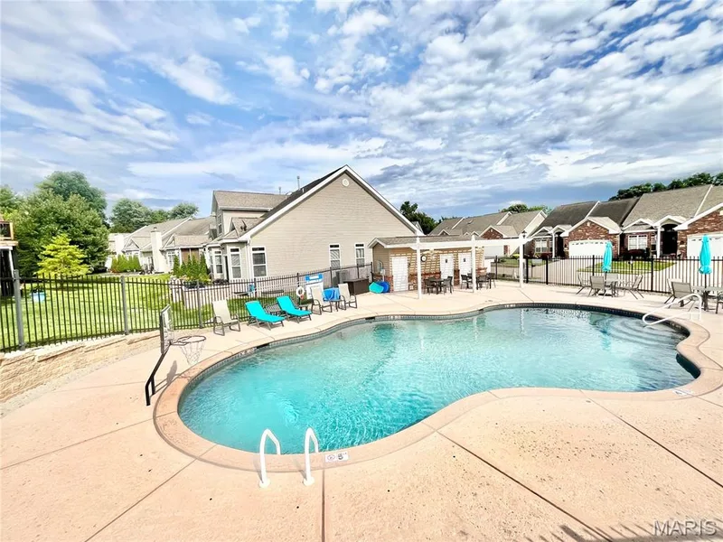 Shaped swimming pool with integrated steps, surrounded by a concrete deck, black metal fencing, and a covered patio area — 197 Woodland Place Court, St Charles, MO 63303