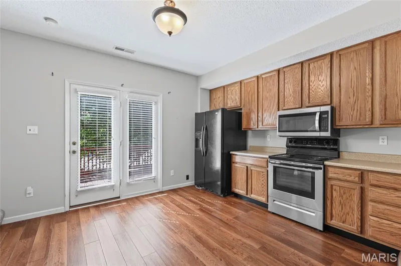 Kitchen featuring wood-finish flooring, wood cabinetry, light-toned countertops, and French doors — 3245 Domain Street, St Charles, MO 63301