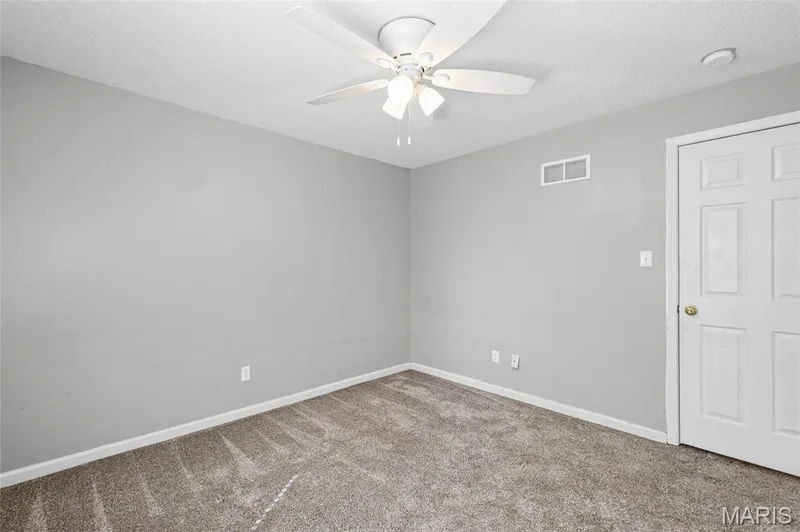 Recessed panel door with brass hardware, light-toned walls, and textured carpet flooring — 3245 Domain Street, St Charles, MO 63301