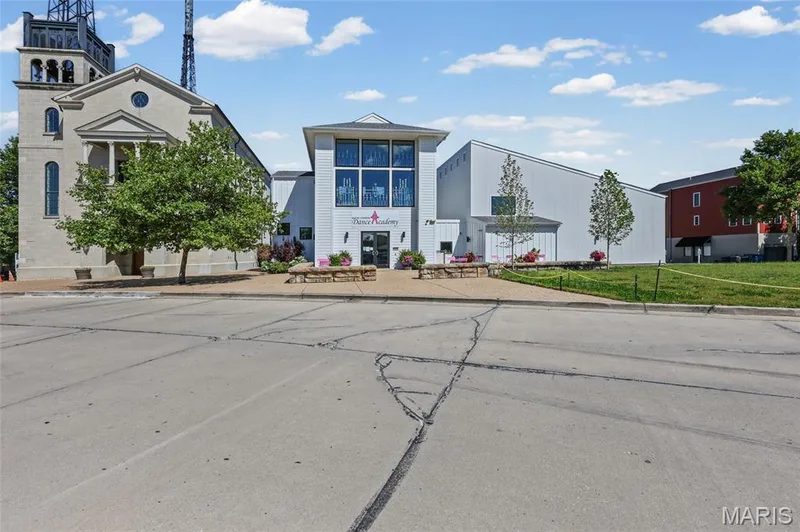Modern commercial building with large storefront windows, stone accents, mature trees, and a landscaped entrance — 3245 Domain Street, St Charles, MO 63301