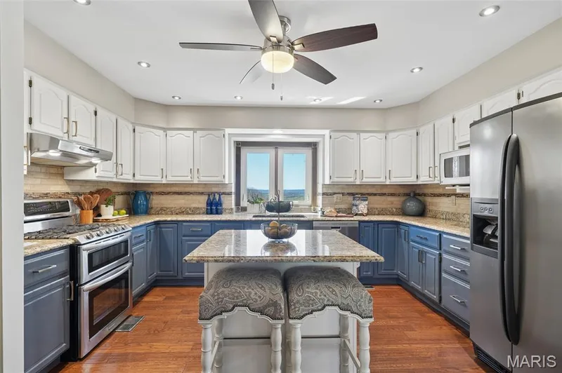 Kitchen with two tone cabinets, stainless steel appliances, light stone counters, ceiling fan, and a breakfast bar — 1553 Ridge Road, Wildwood, MO 63021