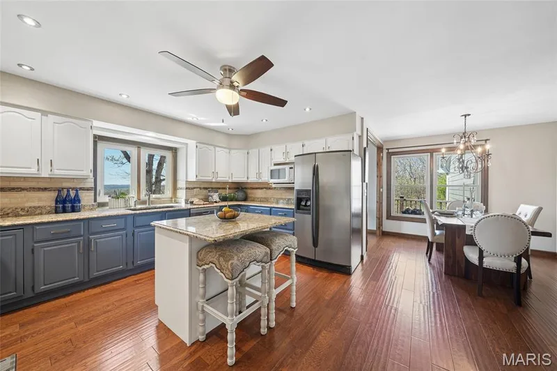 Kitchen with a breakfast bar, dual tone cabinets, stainless steel refrigerator with ice dispenser, light stone counters, and dark wood finished floors — 1553 Ridge Road, Wildwood, MO 63021