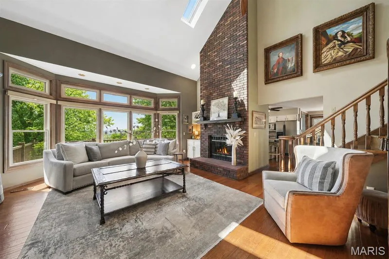 High ceilings with skylight, bay window with multiple panes, brick fireplace with mantel, wood-finish flooring, and a wooden staircase — 1553 Ridge Road, Wildwood, MO 63021
