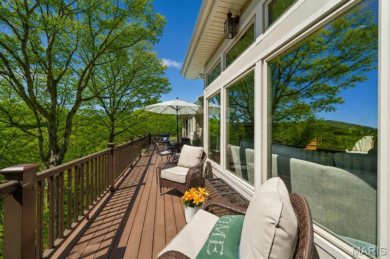 Expansive wood-finish deck with a full-length railing, featuring large windows and an exterior wall light fixture — 1553 Ridge Road, Wildwood, MO 63021