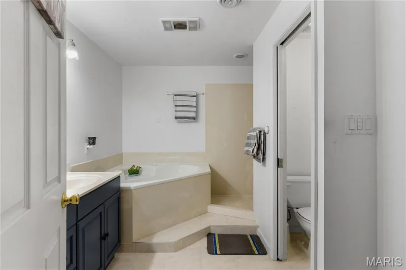 Bathroom featuring vanity, a bath, and light tile patterned flooring — 10107 Greenbriar Court, Foristell, MO 63348
