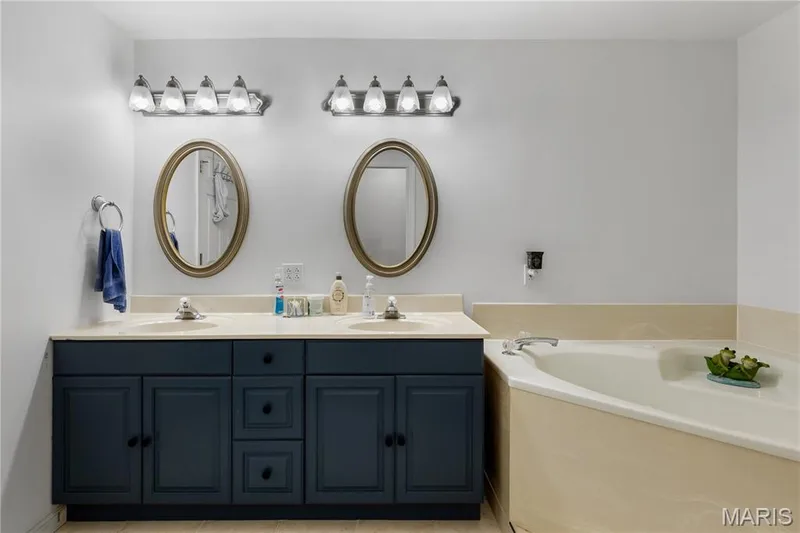 Full bath with double vanity, a bath, and light tile patterned floors — 10107 Greenbriar Court, Foristell, MO 63348