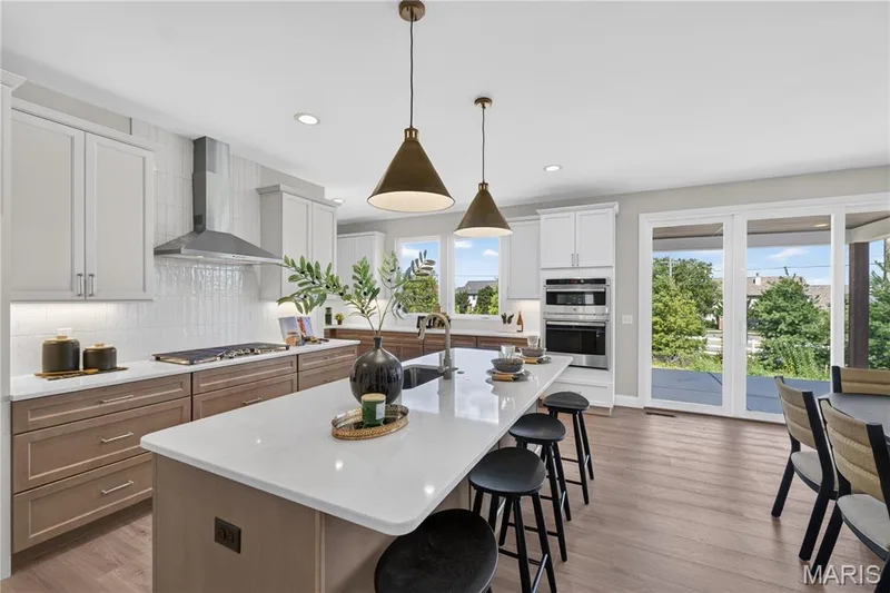 Contemporary kitchen featuring a large central island with seating, a gas range with a stainless steel hood, built-in double ovens, and sliding glass doors opening to an outdoor area — 126 Royal Troon Drive, Dardenne Prairie, MO 63368