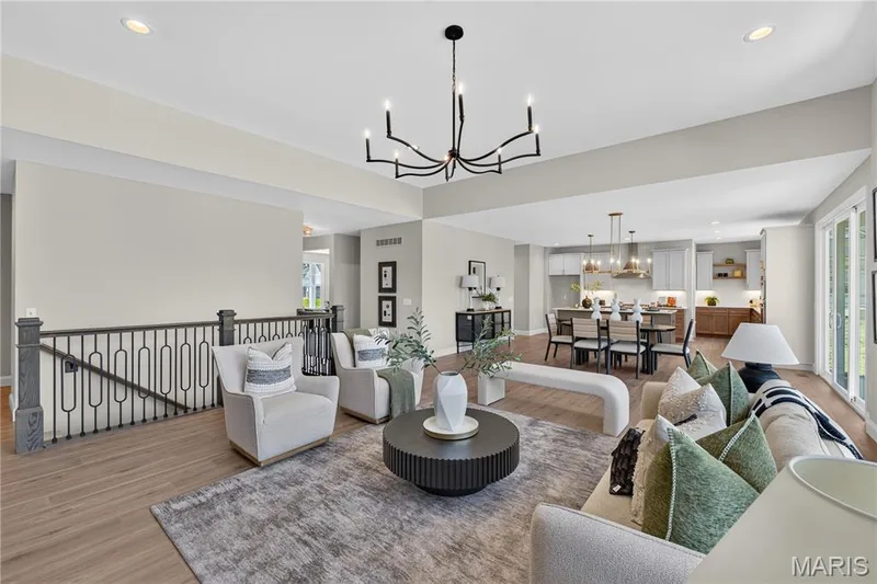 Open-concept Great room featuring a modern chandelier, light wood-finish flooring, recessed lighting, and a wrought iron staircase railing — 126 Royal Troon Drive, Dardenne Prairie, MO 63368