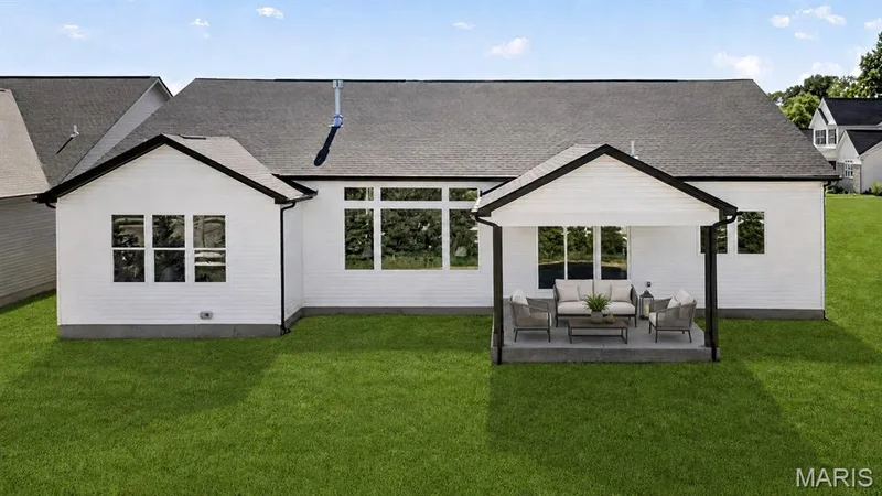 Expansive rear exterior featuring a covered patio with a concrete slab, white siding, black trim, and large windows — 126 Royal Troon Drive, Dardenne Prairie, MO 63368